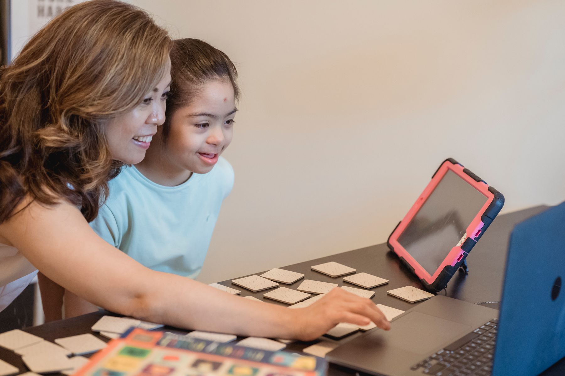 Parent and child using learning cards together beside a laptop